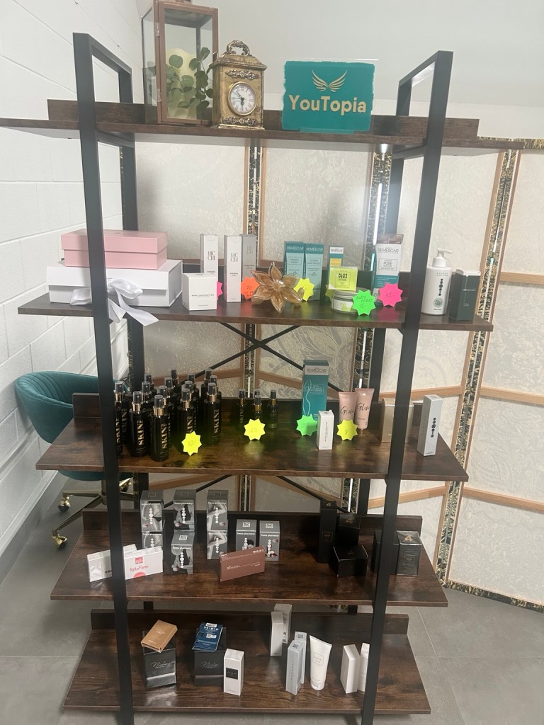 Wooden shelving unit displaying various skincare products with teal YouTopia sign and decorative gold clock