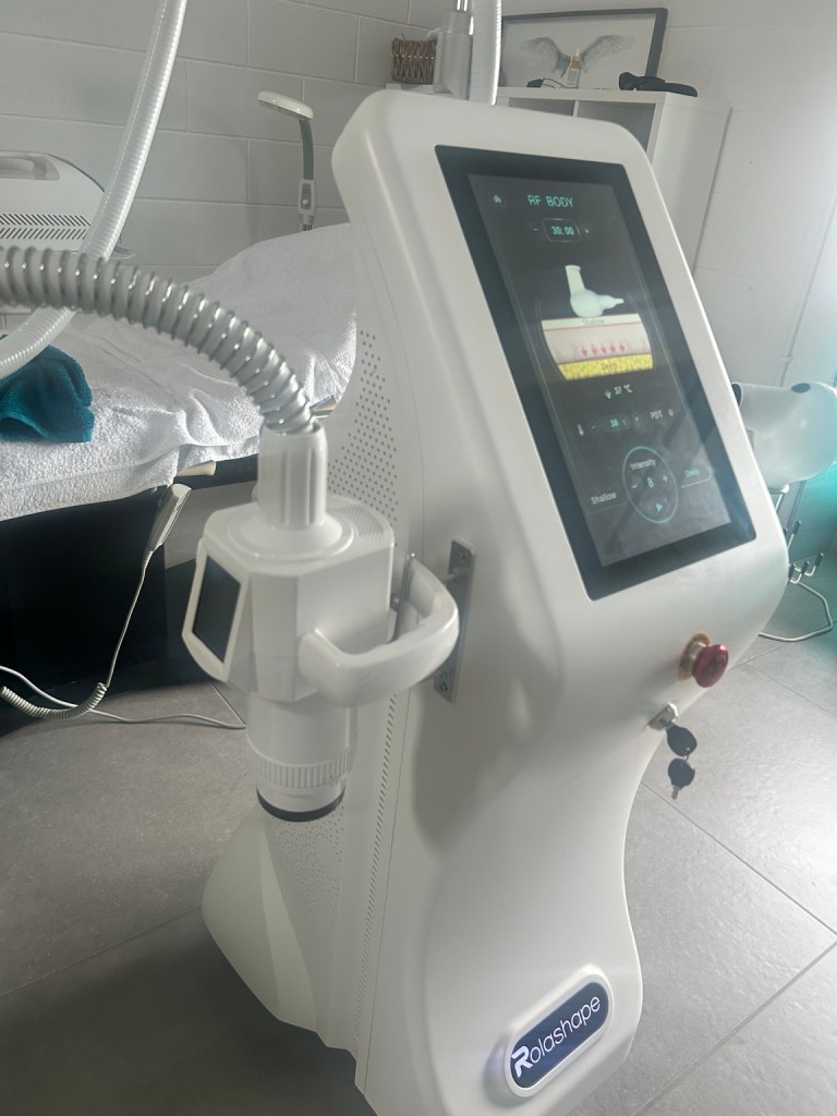 RolaShape body contouring machine with screen and curved arm in clinic treatment room